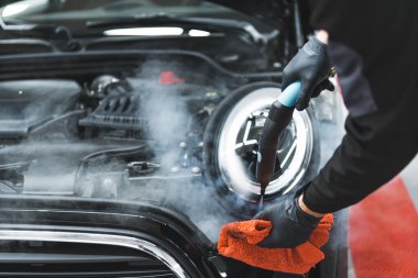 Araba farlarını temizlemek ve dezenfekte etmek için sıcak buhar ve yumuşak bez kullanan profesyonel bir stüdyo çalışanı. Yüksek kalite fotoğraf