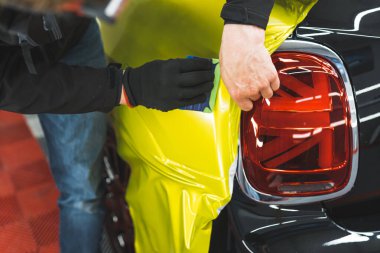 Araba paketleme işleminin yakın çekimi. İki el, siyah bir arabanın yüzeyine neon sarısı plastikler sürüyor. Yüksek kalite fotoğraf