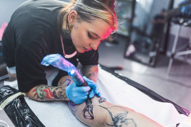 Dövmeci kadın bacağına makine ve eldiven kullanarak dövme yapıyor. Yüksek kalite fotoğraf