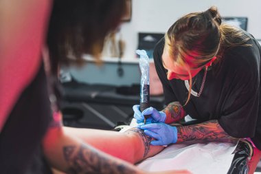 Dövme ustası, insan vücudunu iğne makinesiyle boyuyor, profesyonel kuaförde dövme yapıyor. Yüksek kalite fotoğraf