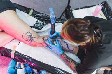 Dövme ustası kız, bir kadının bacağına dövme stüdyosuna büyük bir dövme çiziyor. Yüksek kalite fotoğraf