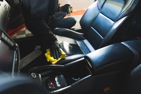 Unrecognizable car detailing expert using cleansing product and yellow microfibre cloth to clean black leather car seat. High quality photo