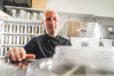 Profesyonel mutfak, paslanmaz çelik ekipman ve siyah üniformalı bir aşçı. İş yerindeki kel beyaz adam doğrudan kameraya bakıyor. Yüksek kalite fotoğraf