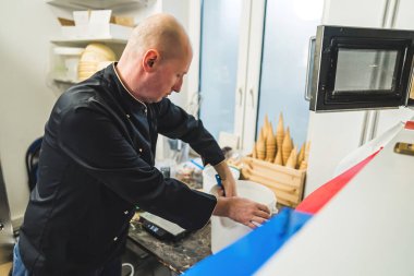 Kapalı alandaki hamur işi aşçının dondurmayı kovaya karıştırması ve mutfakta dondurmalı dondurma külahının yanında durması. Yüksek kalite fotoğraf