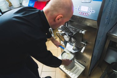 Küçük üretici adam dondurma makinesinden beyaz vanilyalı dondurma alıp metal kovaya koyuyor. Yüksek kalite fotoğraf