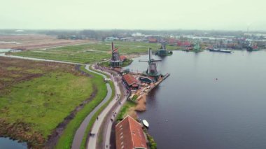 Arka planda bir şehir olan nehir kenarındaki güzel Hollanda yel değirmenlerinin video çekimi. Yüksek kalite 4k görüntü