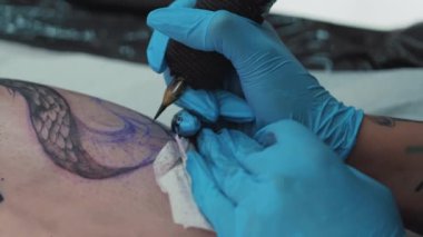Closeup hands of a tattoo artist wearing gloves making a tattoo on clients body. High quality 4k footage