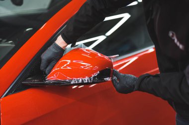 Araba uzmanı, boya ve tamirhaneden korumak için aynaya vinil ambalaj uyguluyor. Yüksek kalite fotoğraf