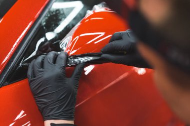 Siyah koruyucu eldivenlerde uzman. Kırmızı bir spor arabanın yan aynasına nazikçe şeffaf araba plastiği yapıştırıyor. Yüksek kalite fotoğraf