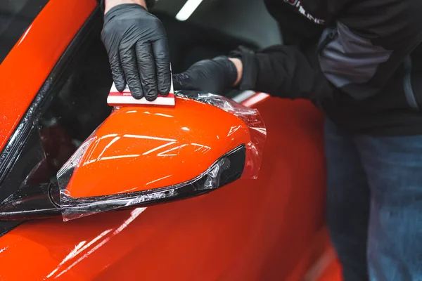 Bir uzman, kırmızı arabaların yan aynalarına vinil ambalaj uyguluyor. Yakın çekim. Yüksek kalite fotoğraf