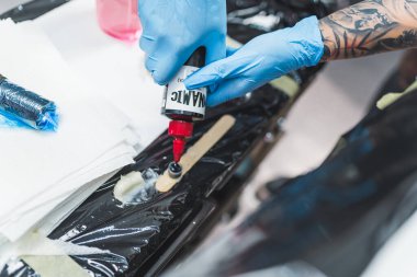 06.06.2023 Varşova, Polonya. Dövme mekanizmasına siyah mürekkep yapıştıran koruyucu lastik eldivenli iki el. Yüksek kalite fotoğraf