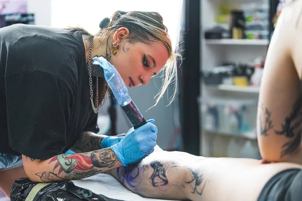 纹身的过程 专注的女性纹身艺术家的室内肖像 画在她最喜欢的女性客户的腿上 是的高质量的照片 — 图库照片