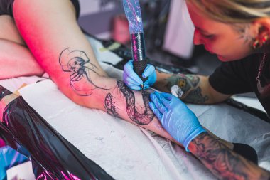 Bacak dövmesi konsepti. Kadın dövmeciler tarafından özel ekipman ve koruyucu eldiven kullanılarak yapılmış vücut sanatı. Yüksek kalite fotoğraf