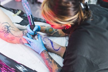 İş sırasında dövmeci bir kızın yüksek açılı perspektifi. Bir müşterinin bacağına dövme çizme işlemi. Yüksek kalite fotoğraf