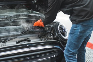 Araba temizleme uzmanı siyah aracı temizliyor ve araba yüzeyini turuncu bir mikrofiber bezle siliyor. Yüksek kalite fotoğraf