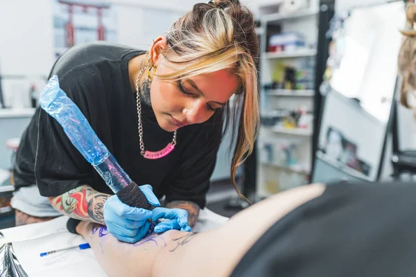 工作时集中精神 白种人女纹身师致力于她的新腿纹身设计 拿着纹身枪的女人高质量的照片 — 图库照片