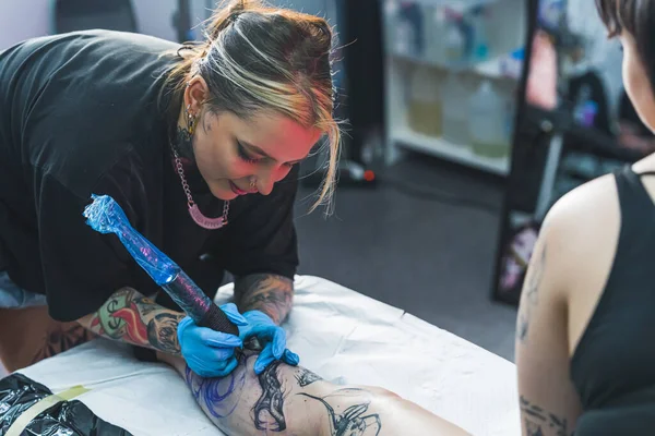 画一个大腿纹身的漫长过程 室内枪击案女性纹身艺术家使用专业的纹身枪在其客户的小腿上画一个纹身 高质量的照片 — 图库照片