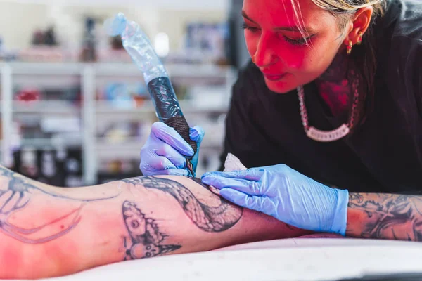 Indoor portrait of a female artist drawing a tattoo on a clients leg. Blurred background. Tattooing process copy space. . High quality photo