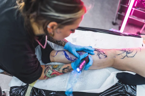女纹身艺术家在客户腿上画纹身 概念艺术 高角度室内射击 模糊的背景 高质量的照片 — 图库照片