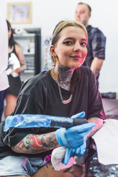 微笑积极的女性纹身艺术家在做纹身时看着相机 模糊的背景 纹身工作室的广告 垂直室内拍摄 高质量的照片 — 图库照片
