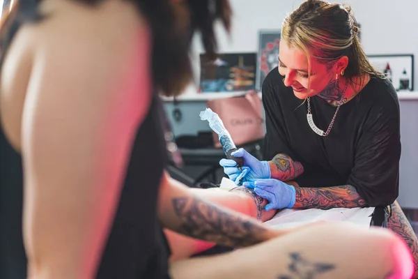 Portrait of a laughing happy woman tattoo master showing a process of creation tattoo on a leg. Positive work environment. High quality photo