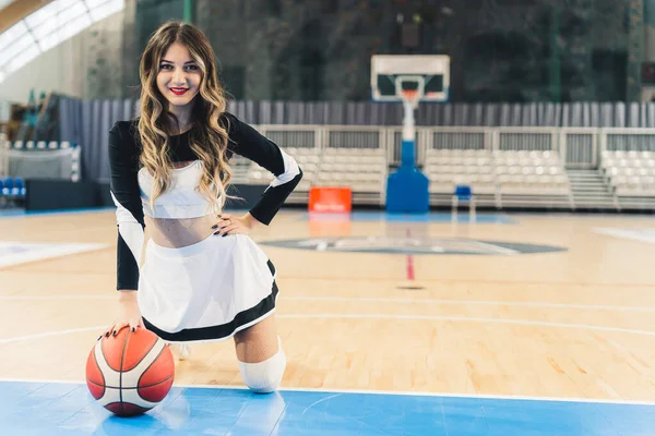 Elinde basketbol topuyla, dizlerinin üzerinde gülümseyen beyaz bir ponpon kız. Yüksek kalite fotoğraf