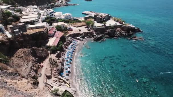 美しいギリシャのフィニカスビーチルートの空中スローモーションビュー 傘と観光客でいっぱいの岩場近くの小さなビーチ 高品質の4K映像 — ストック動画