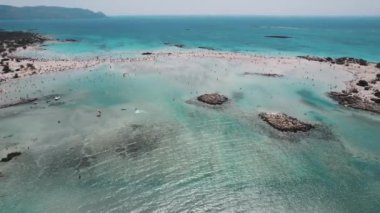 Onlarca turist Elafonisi sahilinde geziniyor ve harika bir yaz tatili, temiz su ve yaz etkinlikleri geçiriyorlar. Yüksek kalite 4k görüntü