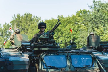 16.08.2023 Varşova, Polonya. Bir makineli tüfeğin önünde modern askeri aracın üzerinde duran odaklanmış zırhlı askerin açık hava portresi. Yüksek kalite fotoğraf