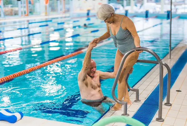 senior woman on the side of a pool helping her husband to come out from the pool. High quality photo