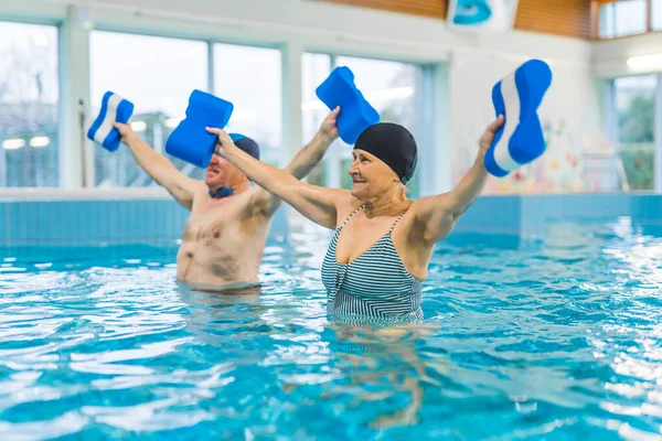 Senior man and woman doing aerobic water exercises in the swimming pool. High quality photo