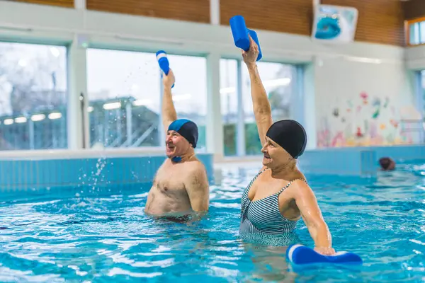 Grandparents taking care of their health. Senior adult caucasian married couple doing aqua fitness exercises with pool buoys. High quality photo