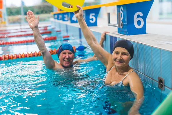 Stock image positive energetic caucasian senior couple submerged in turquoise swimming pool water with hands up in the air. Swimming gear and equipment. High quality photo