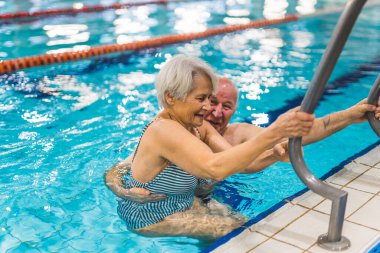 senior man helping his wife to come out from the indoor pool, happy marriage. High quality photo clipart