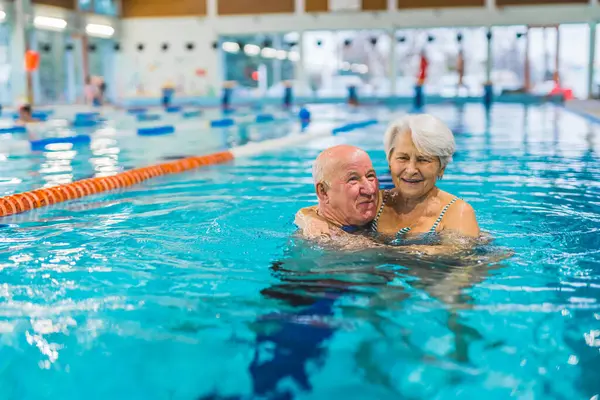 cheerful aged couple hugging each other in the pool and having a great time. High quality photo