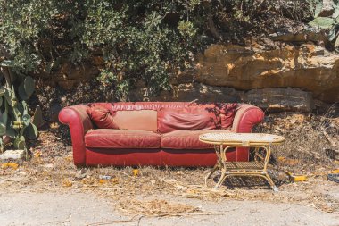 Güneşli bir günde kırmızı, eski, yırtık bir kanepe ve sokakta eski bir masa. Yüksek kalite fotoğraf