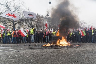 06.03.2024. Varşova, Polonya. İnsanlar protestoda tekerlek yakıyor ve ellerinde bayraklar ve posterlerle ateşin etrafında dikiliyorlar. Yüksek kalite fotoğraf