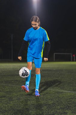 Gece geç saatlerde stadyumda futbol topuyla antrenman yapan mavi üniformalı bir genç. Yüksek kalite fotoğraf