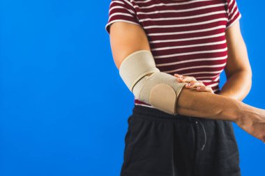 Acıyı azaltmak için dirsek desteği takan kadın, mavi arka plan. Yüksek kalite fotoğraf