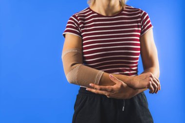 Bilinmeyen bir kadın mavi arka planda dirseğinde bandaj gösteriyor. Yüksek kalite fotoğraf
