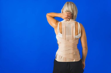 Sırt korsesi takmış genç bir kadın mavi arka planda dikiliyor, orta boy arka görüş fotokopi alanı. Yüksek kalite fotoğraf