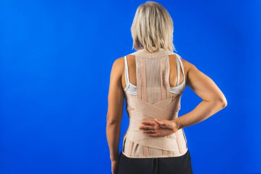 Ortopedik bel korsesi olan sarışın bir kadın mavi arka plan üzerinde poz veriyor. Yüksek kalite fotoğraf