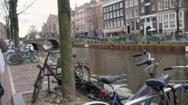 Bulutlu Amsterdam caddelerinde yürüyor, Hollanda 'da kanalların yakınında bisikletler sürüyor. Yüksek kalite 4k görüntü