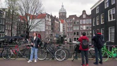 12.03.2024. Amsterdam, Hollanda. Amsterdam 'daki bina ve kanalların fotoğraflarını çeken turistler ve Hollanda, Amsterdam' daki köprüde parketmiş bisikletliler. Yüksek kalite 4k görüntü