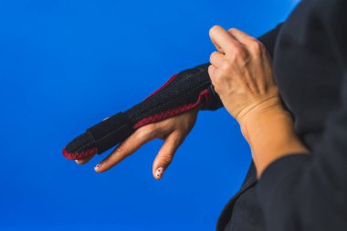 Orta parmağındaki alçıyı düzelten bir kadın, yaralı bir parmak mavisi arka plan. Yüksek kalite fotoğraf