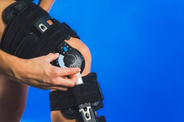 Sargı bezi sıkıştırma açısını ayarlayan bir kadının yakın plan çekimi mavi arka plan, sağlık konsepti üzerine dizlik takması. Yüksek kalite fotoğraf