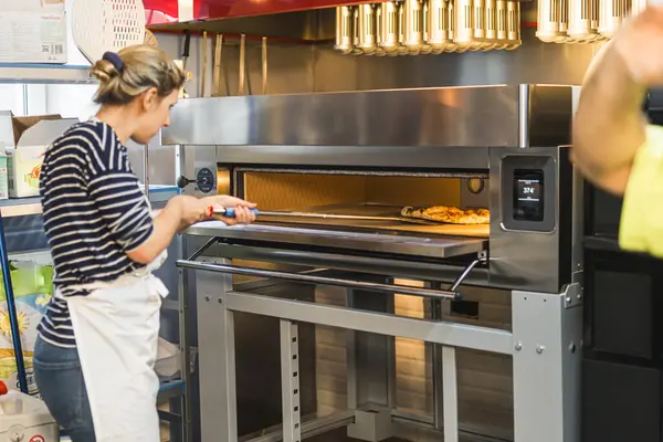 Kadın aşçı pizzayı elektrikli fırına koyup İtalyan yemeği hazırlıyor. Yüksek kalite fotoğraf