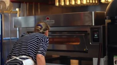 04.04.2024. Varşova, Polonya. Önlüklü kadın pizzayı kabuklu elektrikli fırına koyuyor, restoranın mutfağında çalışıyor. Yüksek kalite 4k görüntü