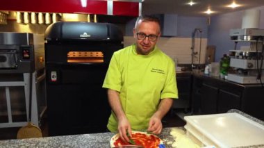 04.04.2024. Varşova, Polonya. Yeşil üniformalı şef pizzacı mutfağında pizza hazırlıyor, İtalyan mutfağında. Yüksek kalite 4k görüntü