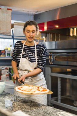 Genç bayan aşçı pizzayı fırına, pastaya ve İtalyan yemek konseptine koymaya hazır. Yüksek kalite fotoğraf